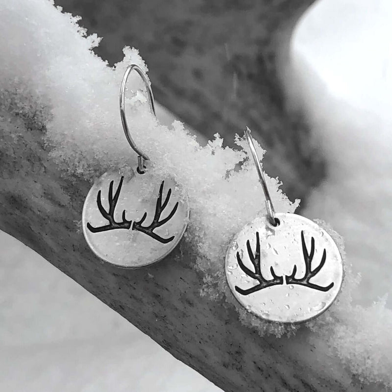 Antler Earrings design featuring etched brass discs with antler motif, showcased on a snowy background.