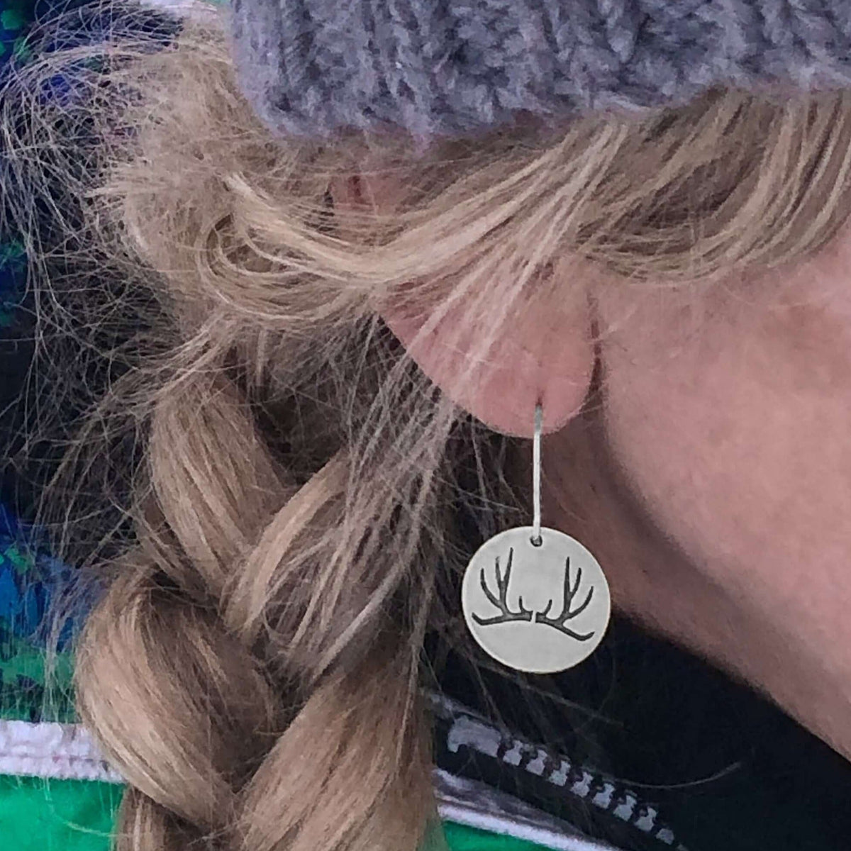 Antler Earrings showcased on a model, featuring etched antlers on brass discs, worn with a knitted beanie.