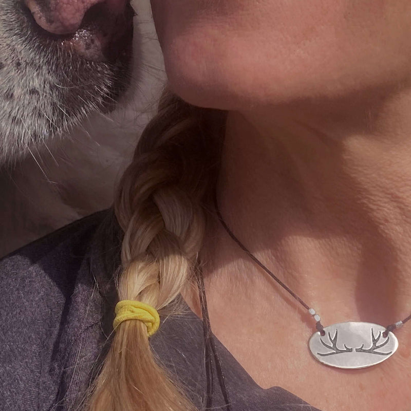 Antlers Necklace worn by a woman with a dog, showcasing its elegant oval shape and nature-inspired design.
