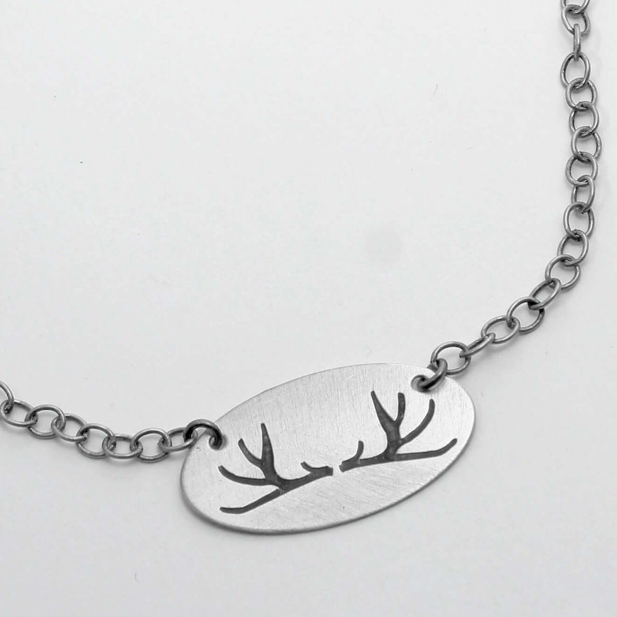 Antlers Necklace featuring a simple, elegant thin oval pendant with antler etchings on a silver chain.