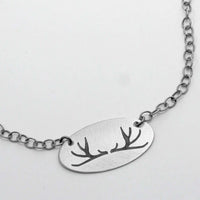 Antlers Necklace featuring a simple, elegant thin oval pendant with antler etchings on a silver chain.