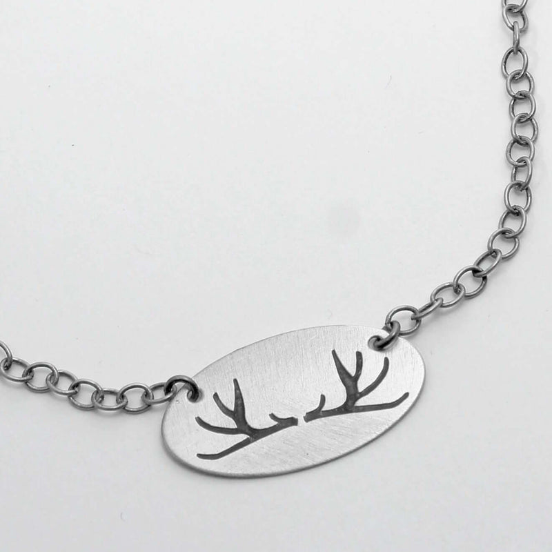 Antlers Necklace featuring a simple, elegant thin oval pendant with antler etchings on a silver chain.