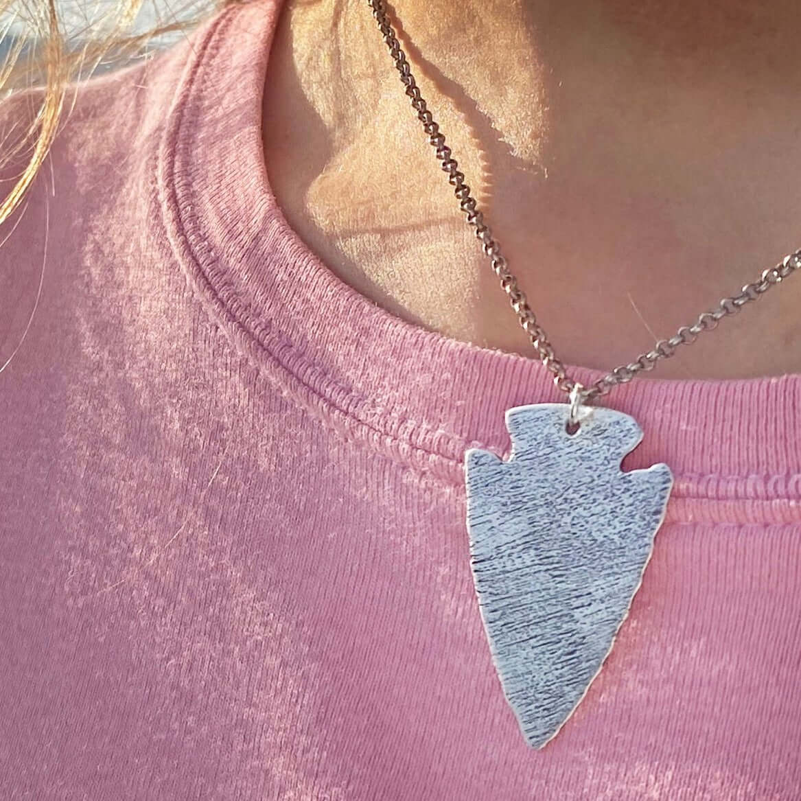 Close-up of Arrowhead Long Layered Necklace in Matte Silver worn on pink shirt, symbolizing courage and strength.