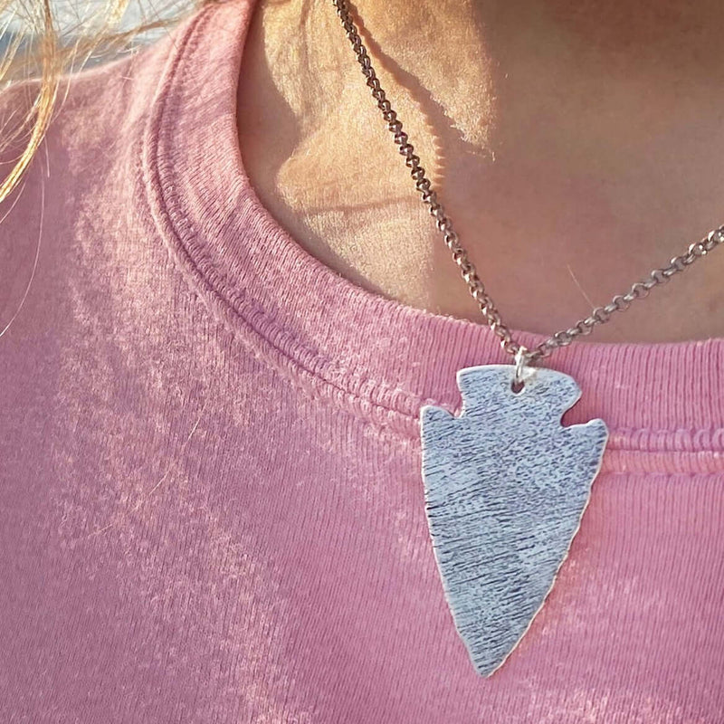 Close-up of Arrowhead Long Layered Necklace in Matte Silver worn on pink shirt, symbolizing courage and strength.