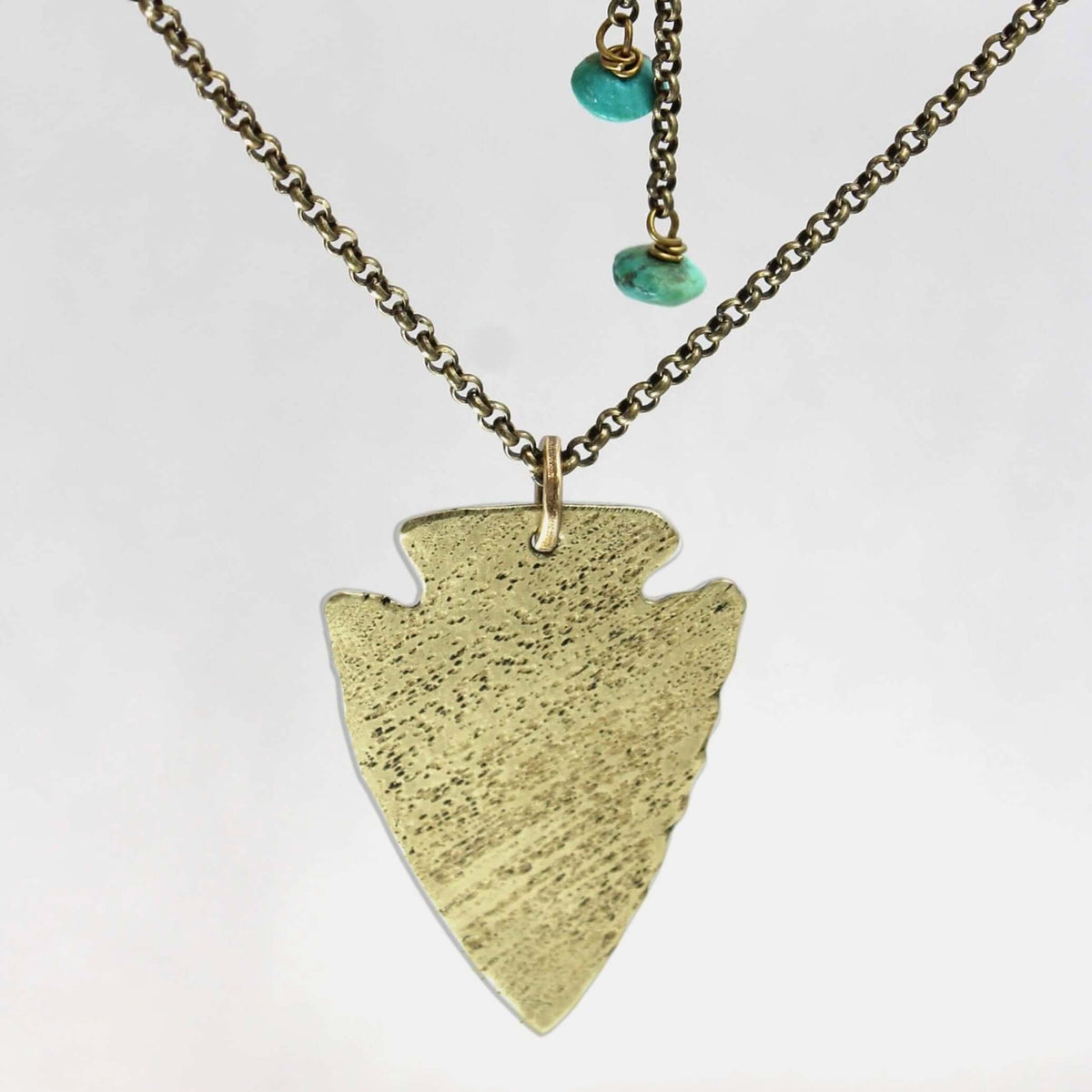Arrowhead Long Layered Necklace featuring a gold arrowhead pendant on a chain with turquoise beads.