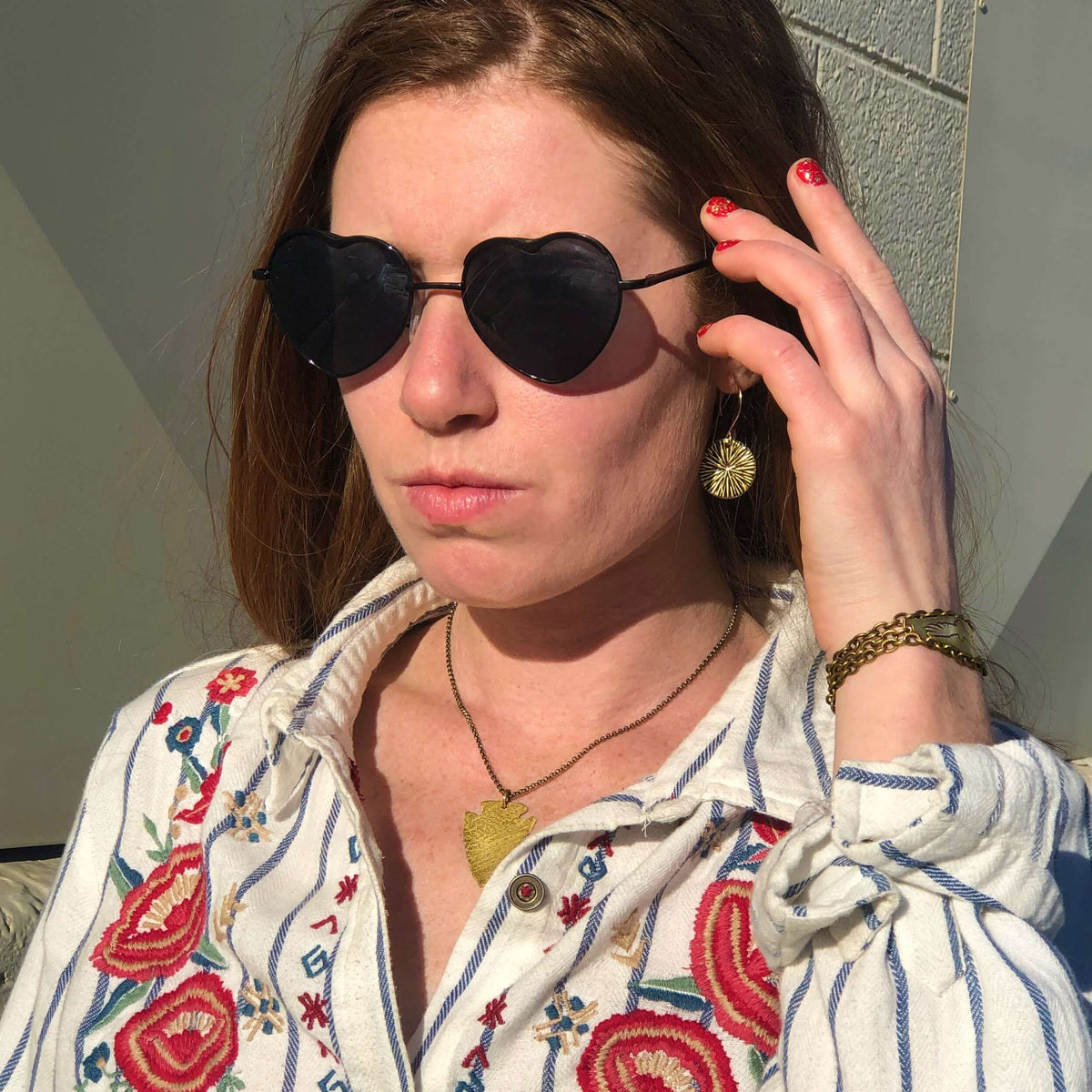 Model wearing Arrowhead Long Layered Necklace with heart-shaped sunglasses and embroidered shirt.