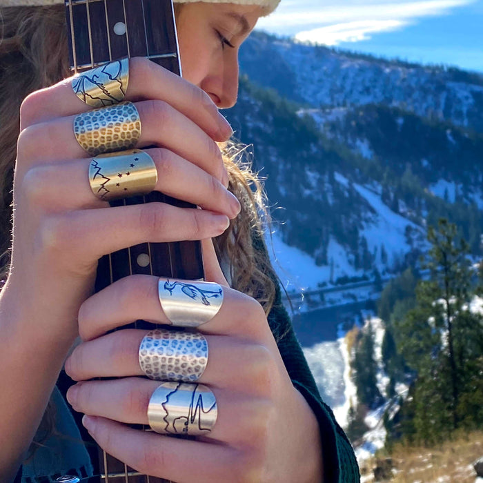A person wearing multiple Big Dipper Adjustable Rings while holding a guitar in a winter landscape.