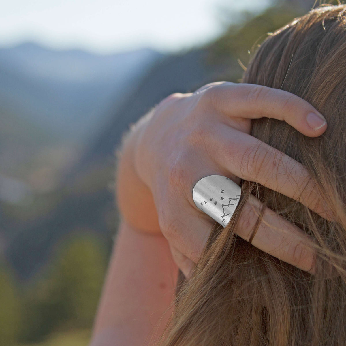 Person wearing a Big Dipper Adjustable Ring outdoors, evoking the beauty of the night sky with mountains in the background.
