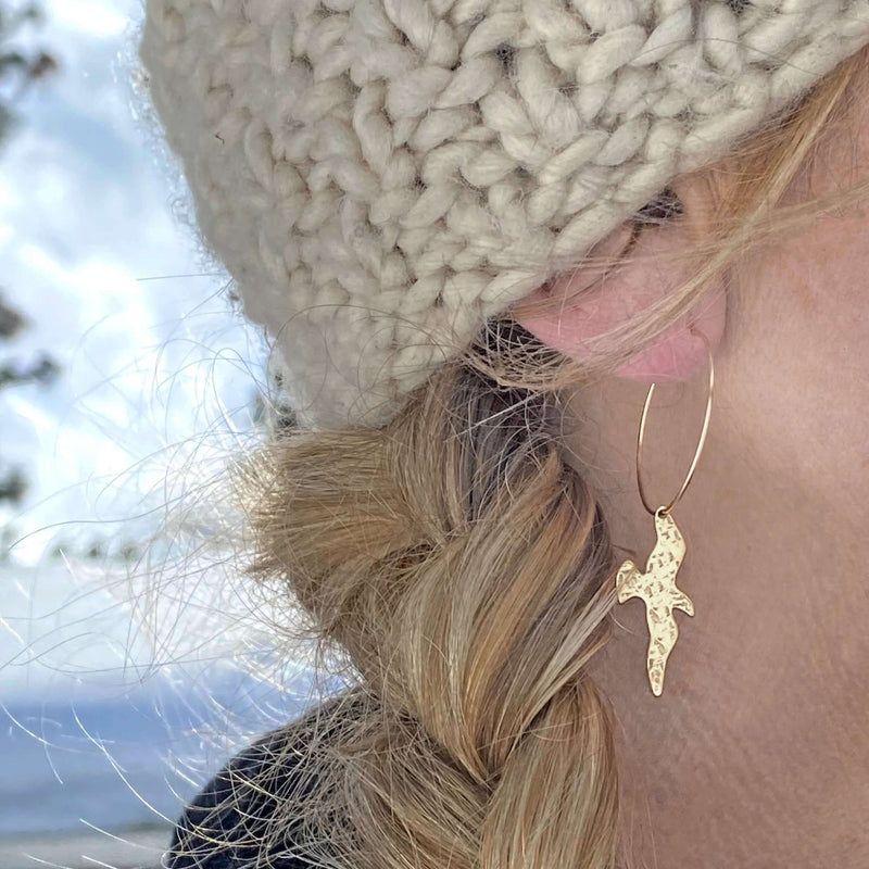Birds on a Wire Hoop Earrings worn by a woman showing a close-up of the gold bird design and delicate hoop.