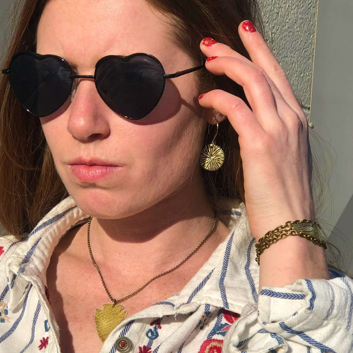 Woman wearing heart-shaped sunglasses and Blossom Earrings in a sunny outdoor setting.