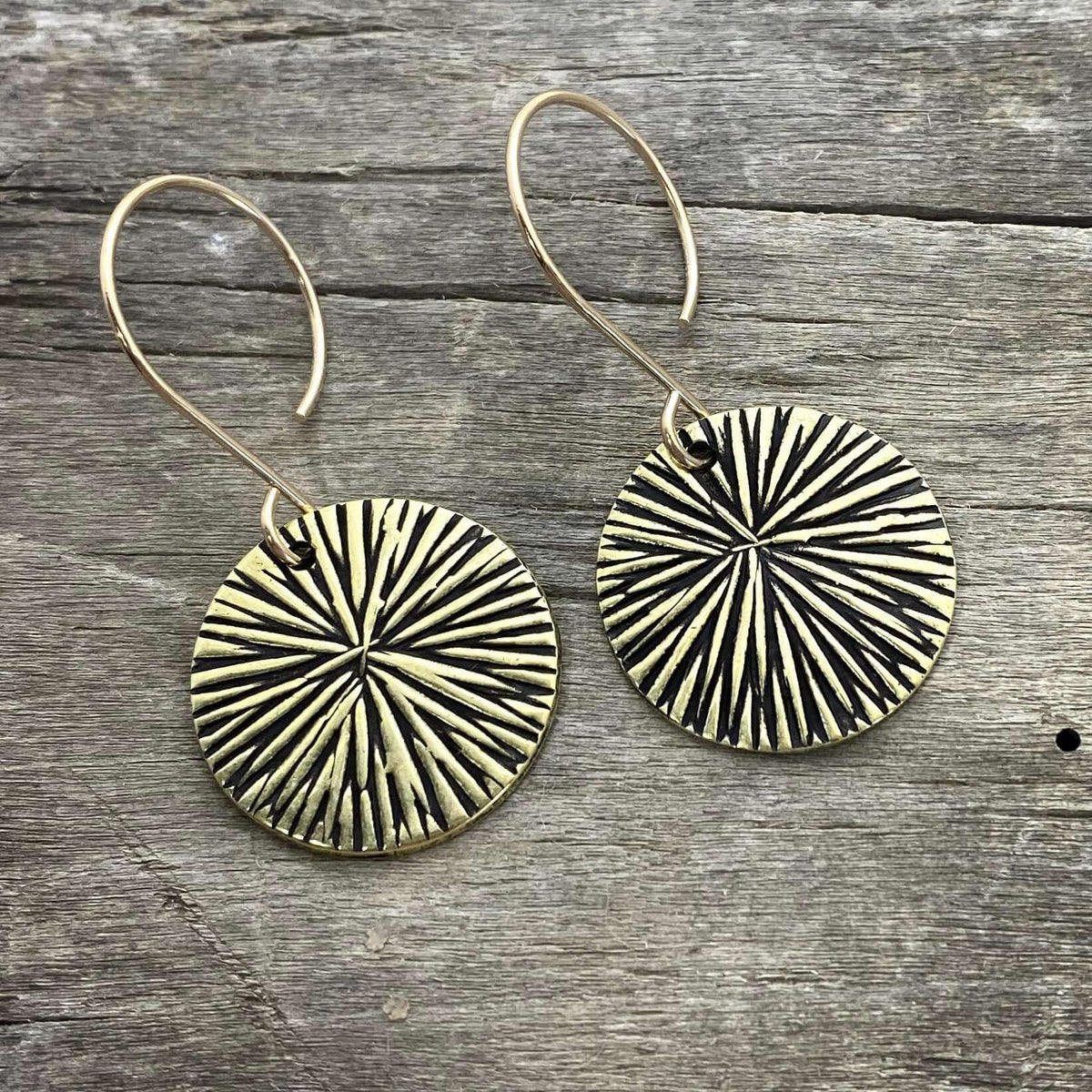 Blossom Earrings featuring modern design with textured discs in antique brass finish on wooden background.