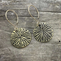 Blossom Earrings featuring modern design with textured discs in antique brass finish on wooden background.