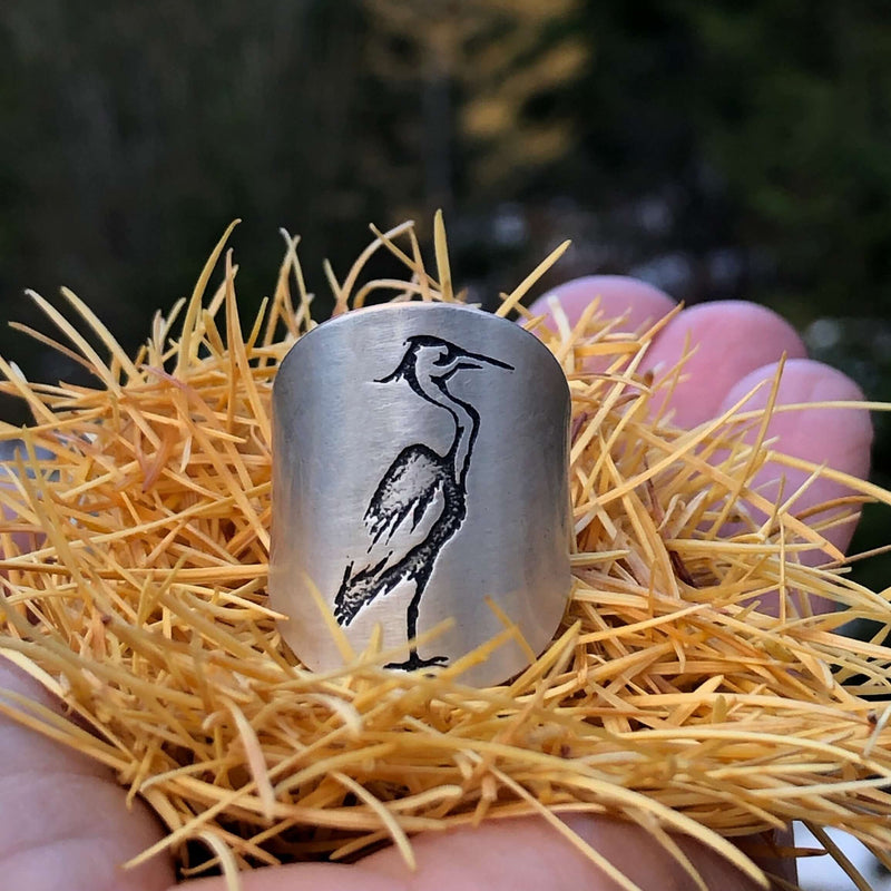 Blue Heron Adjustable Ring displayed on a hand, showcasing the etched great blue heron design on a 1" wide ring.