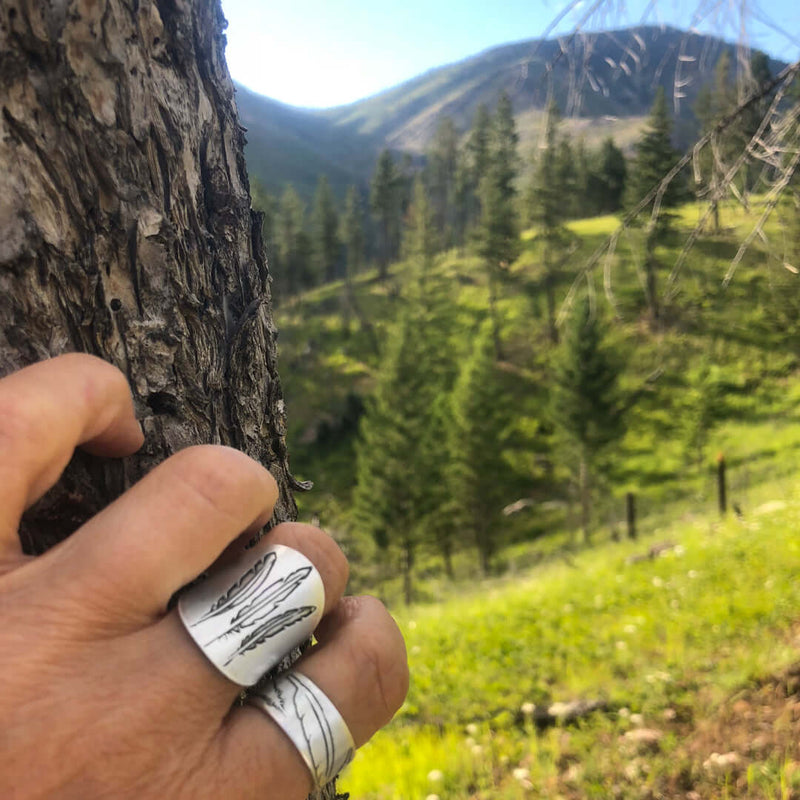 Person wearing a Feather Adjustable Ring while holding a tree in a scenic outdoor setting.