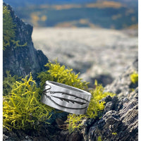 Feather Ring displayed on a mossy surface outdoors, showcasing its intricate feather design in Matte Silver finish.