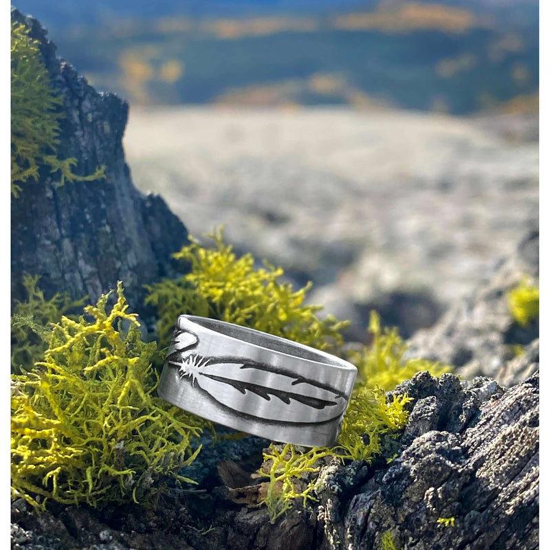 Feather Ring displayed on a mossy surface outdoors, showcasing its intricate feather design in Matte Silver finish.