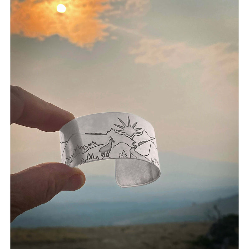Going to the Sun Road Cuff Bracelet showcasing mountains and sun goat against a scenic backdrop.