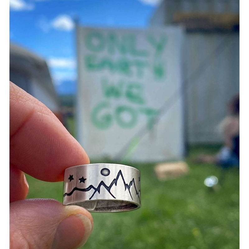 High Alpine Adjustable Ring showcased in hand, featuring mountain and star design with a backdrop of a sign.