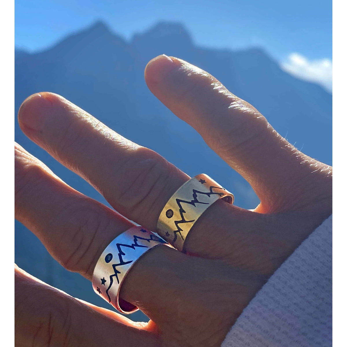 High Alpine Adjustable Ring showcased on hand against mountain backdrop in silver and brass finishes.