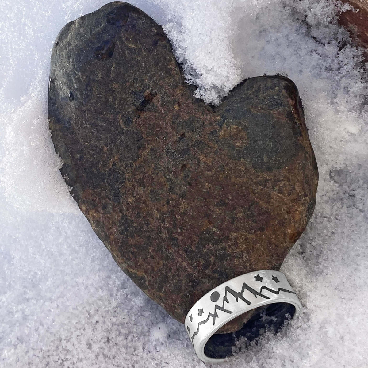 High Alpine Adjustable Ring resting on a heart-shaped rock in snow, showcasing nature-themed design.