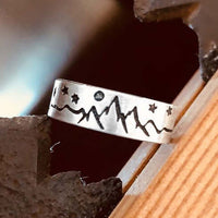 High Alpine Mountain Ring with mountain and star design in matte silver finish, showcased on wood background.