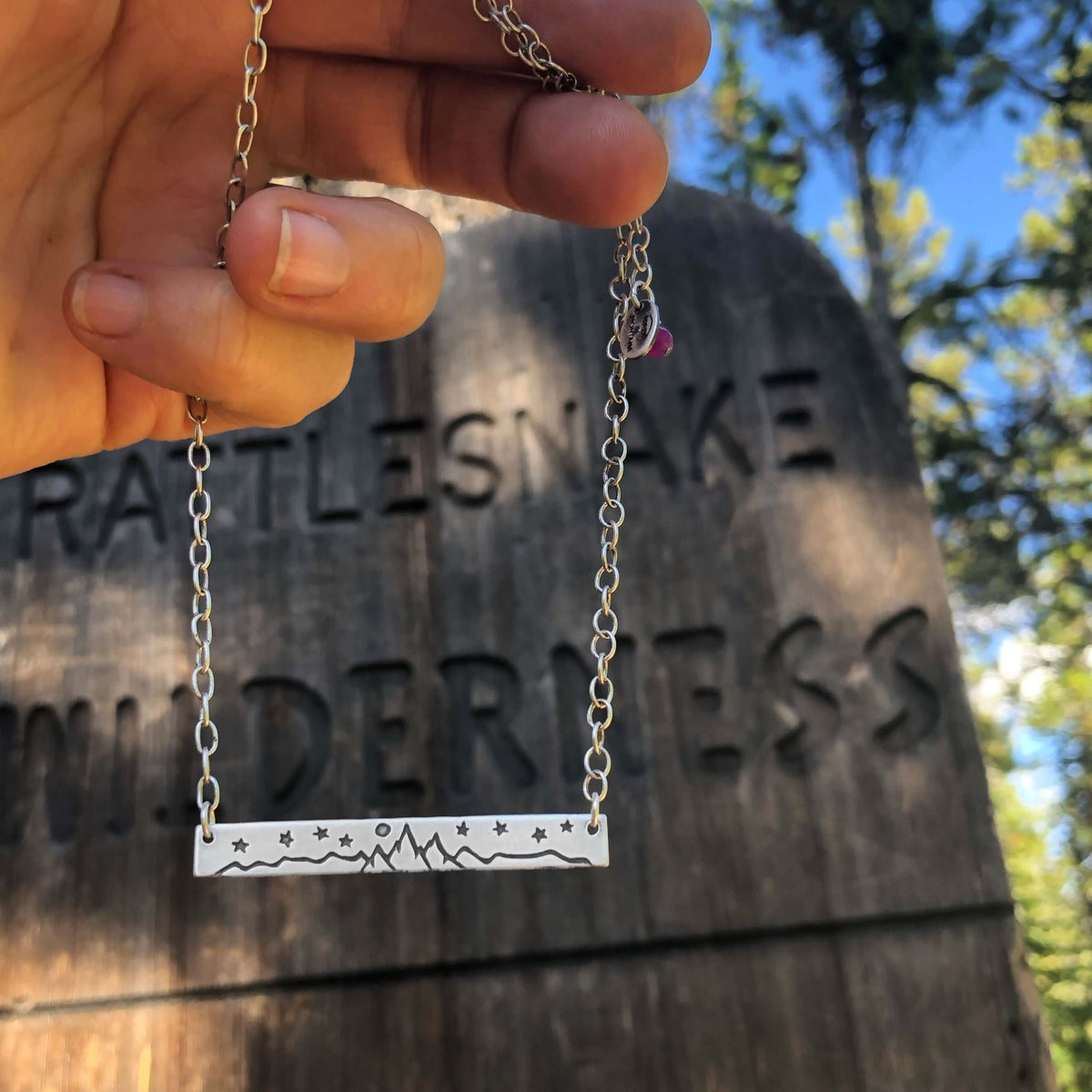 High Alpine Necklace showcased against a wilderness sign, featuring a scenic mountain design in silver.
