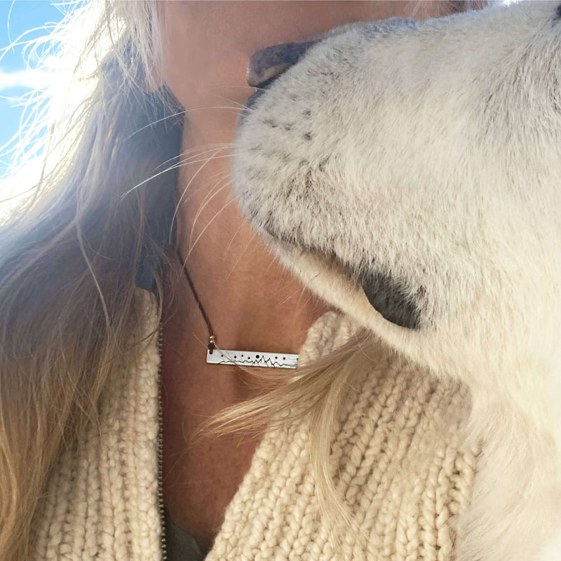 Close-up of High Alpine Necklace worn with a cozy sweater, featuring a dog's affectionate nuzzle.