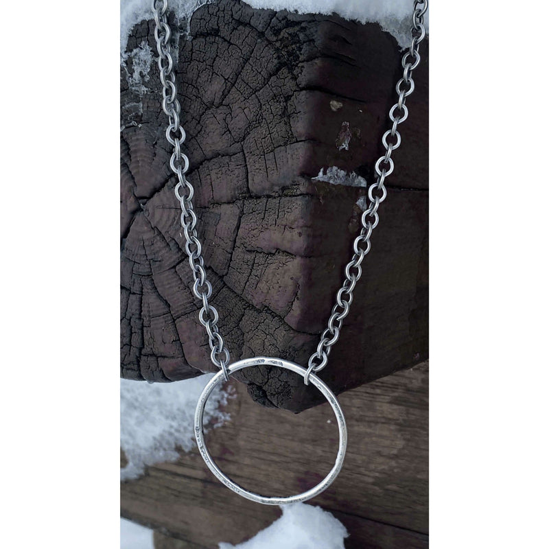 Hula Necklace featuring a silver-coated circle hoop on a chain, displayed against a rustic wooden background.