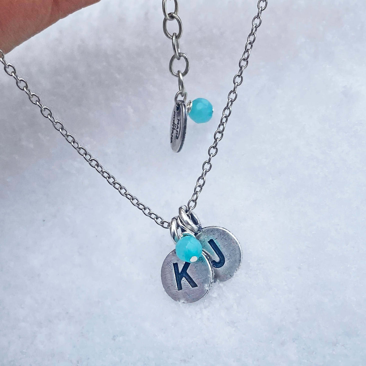 Initial Necklace with custom KU initials and turquoise bead on silver chain in snow.