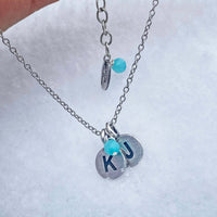 Initial Necklace with custom KU initials and turquoise bead on silver chain in snow.