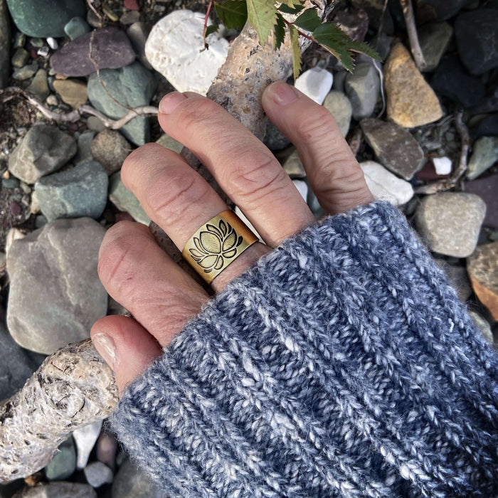 Lotus Adjustable Ring worn by a hand on a rocky background, showcasing unique lotus etching and brass finish.