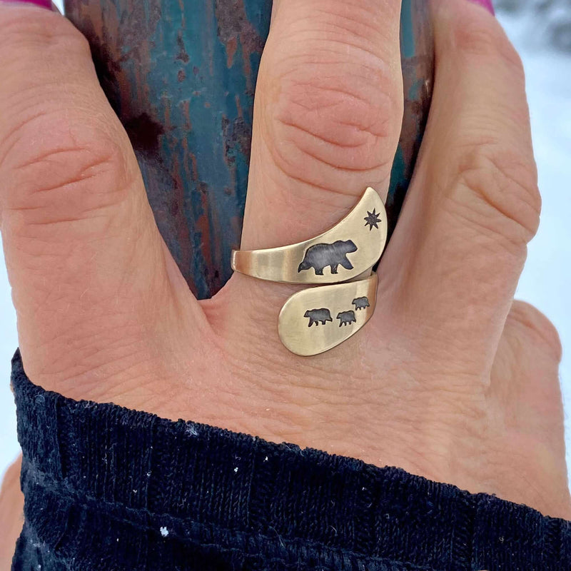 Mama and Cubs Adjustable Ring showcasing a bear design in antique brass finish on a hand against a snowy backdrop.