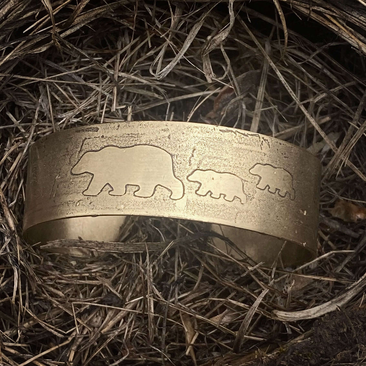 Mama and Cubs Cuff Bracelet resting on nest-like material, showcasing unique bear designs etched in brass.