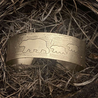 Mama and Cubs Cuff Bracelet resting on nest-like material, showcasing unique bear designs etched in brass.