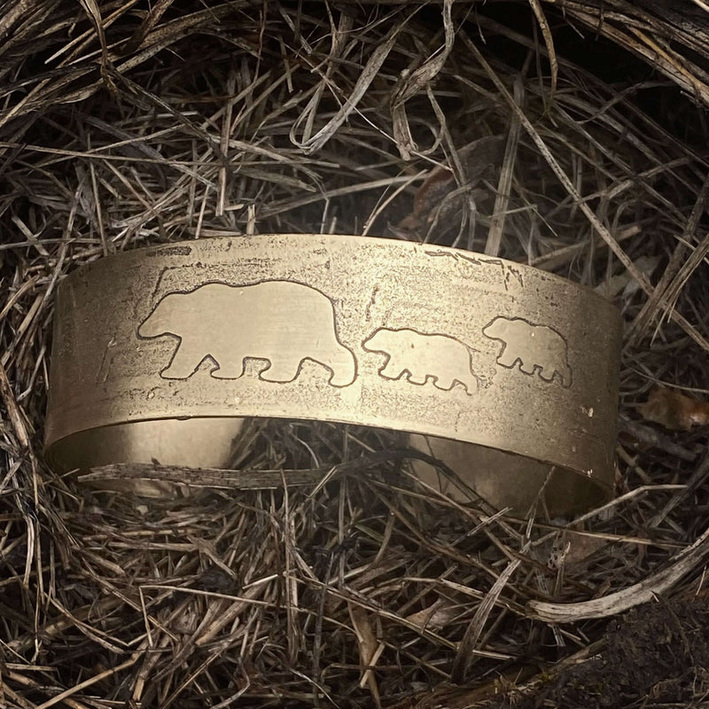 Mama and Cubs Cuff Bracelet resting on nest-like material, showcasing unique bear designs etched in brass.