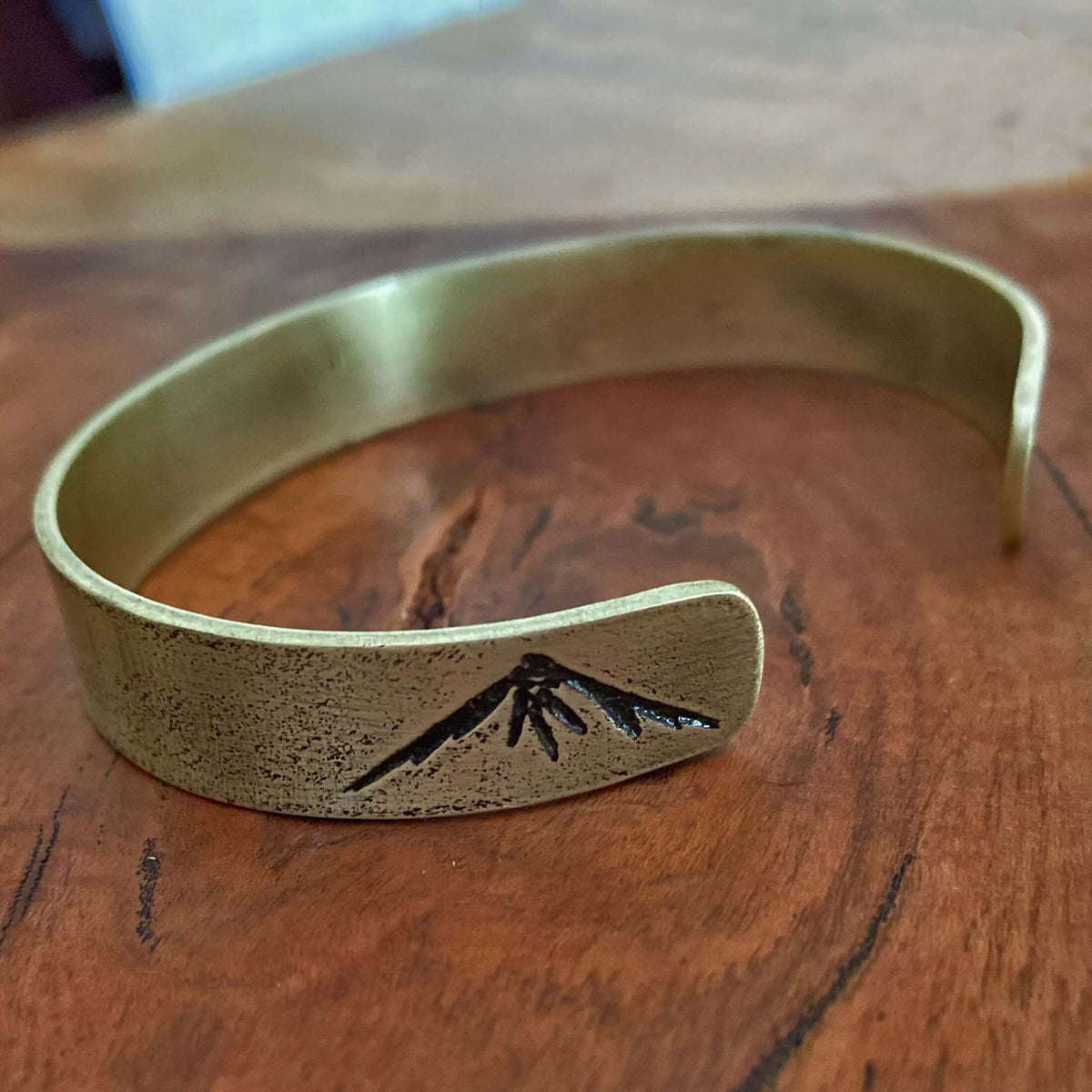 Mountain Peaks Cuff Bracelet displayed on wooden surface, showcasing engraved mountain peaks design.