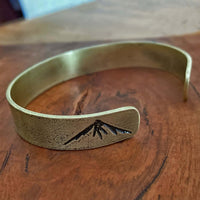 Mountain Peaks Cuff Bracelet displayed on wooden surface, showcasing engraved mountain peaks design.
