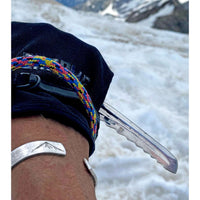 Person wearing the Mountain Peaks Cuff Bracelet on their wrist, set against a snowy mountain background, showcasing outdoor adventure style.