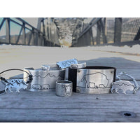 Mountains on Buffalo Necklace and assorted bison-etched jewelry displayed on a wooden surface.