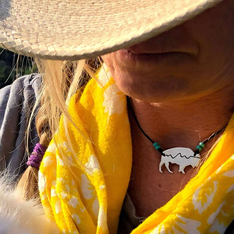 Mountains on Buffalo Necklace worn with a yellow scarf and hat, featuring a bison silhouette.