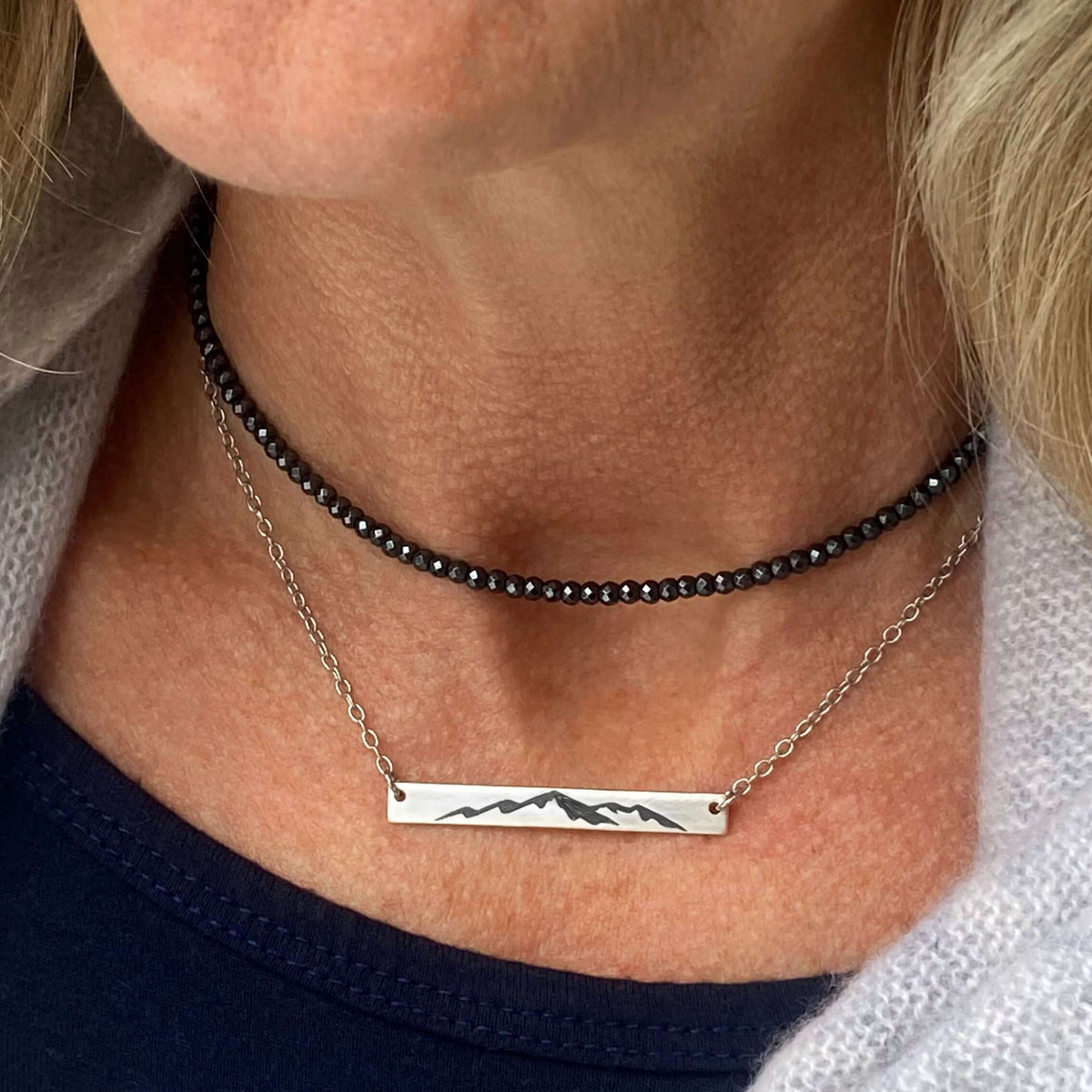 Mountainscape Necklace showcased on a model featuring a mountain silhouette on a cable chain with black beads.