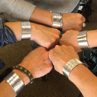 Hands wearing Nordic Run Cuff Bracelet showcasing together, with etched Nordic skier design, perfect for outdoor adventure.