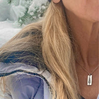 Close-up of a woman wearing a Pine Tree Necklace against a snowy background, showcasing its elegant design.