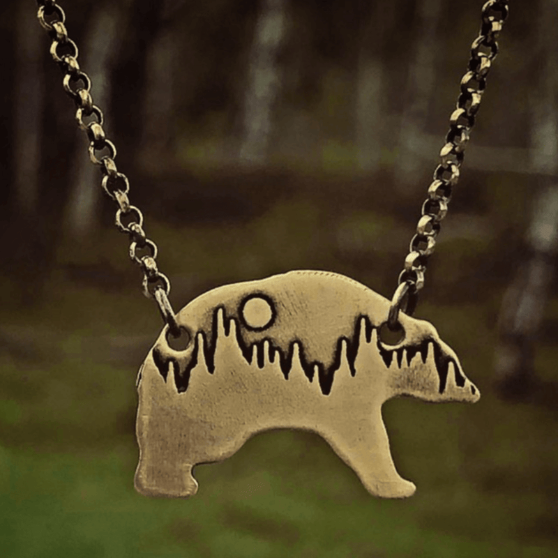 Poya Bear Necklace featuring an etched bear silhouette with a tree line and sun, made from raw brass.