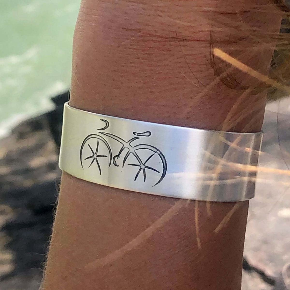 Ride Bicycle Cuff Bracelet featuring a bicycle design on a silver cuff worn on a wrist by a cyclist.