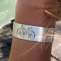 Ride Bicycle Cuff Bracelet featuring a bicycle design on a silver cuff worn on a wrist by a cyclist.