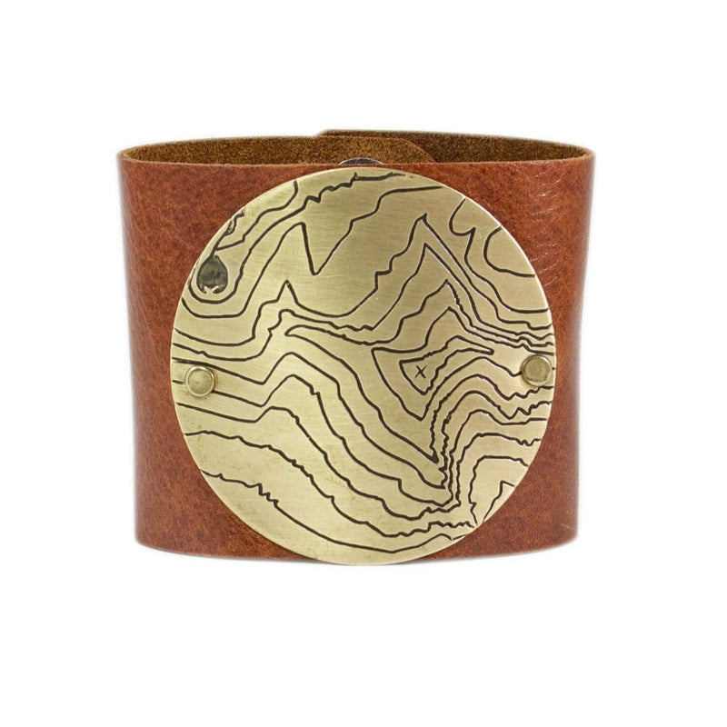 Rising Wolf Disk Leather Cuff featuring a brass topographical disk on a brown leather band.