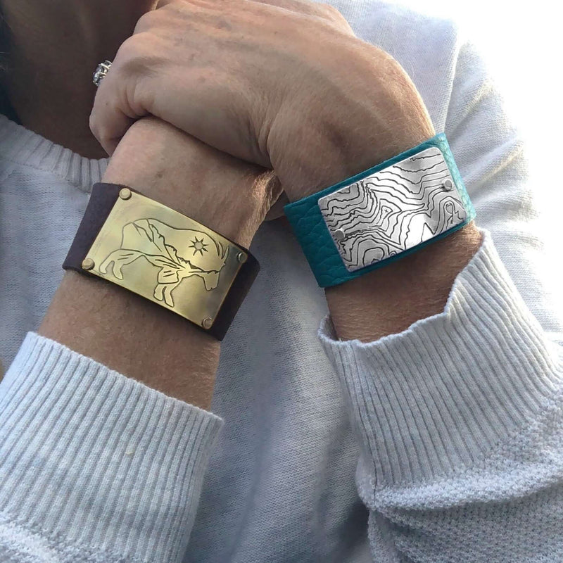 Rising Wolf Leather Cuff Bracelet in matte silver and antique brass finishes, showcasing topographic designs on leather.