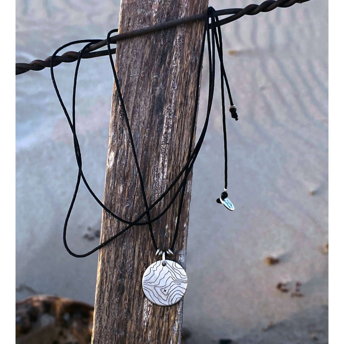 Rising Wolf Necklace displayed on a wooden post, showcasing its intricate topographic design and natural beauty.