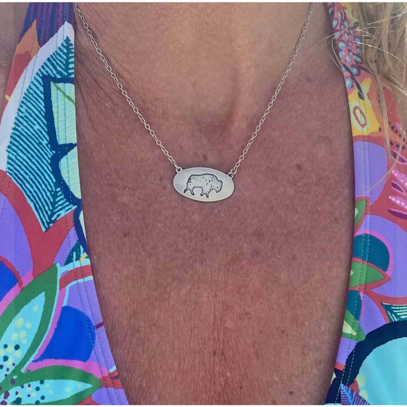 Close-up of a person wearing the Roam Free Necklace featuring a buffalo pendant on a silver chain.